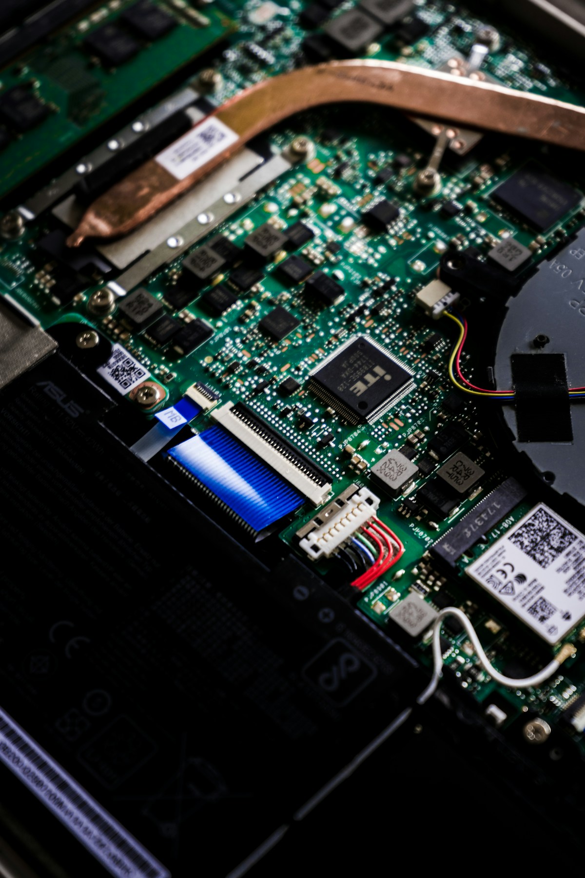 Real laptop motherboard showing fully assembled PCBA with ICs, capacitors, connectors, and heat pipe